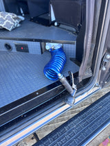 Inside an RV rental: a blue coiled hose and spray nozzle, connected to an internal water hookup for cleaning.
