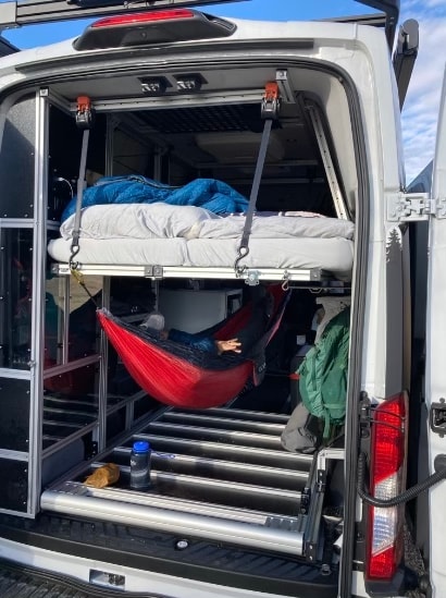 Customized RV rental interior features a suspended bed above a red hammock with a person relaxing, optimizing space. — photo 8