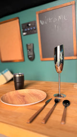 Ready for your RV rental journey! A modern dining setup with wooden plate, cutlery, and sleek silver goblet on a table, with a teal wall backdrop.