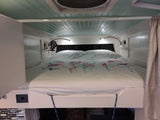 RV rental bedroom featuring a comfy bed with colorful floral duvet, bright reading lights, & a small fan.