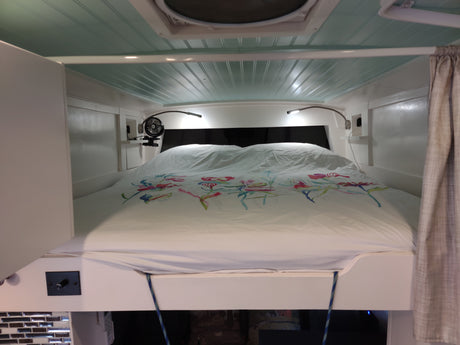 RV rental bedroom featuring a comfy bed with colorful floral duvet, bright reading lights, & a small fan.