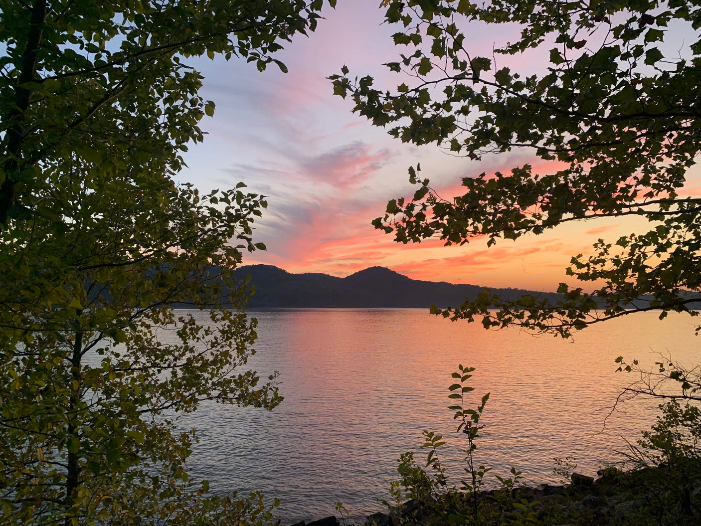 Sunset over a mountain lake, framed by trees. Find your serene RV rental escape to views like this!