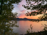 Sunset over a mountain lake, framed by trees. Find your serene RV rental escape to views like this!
