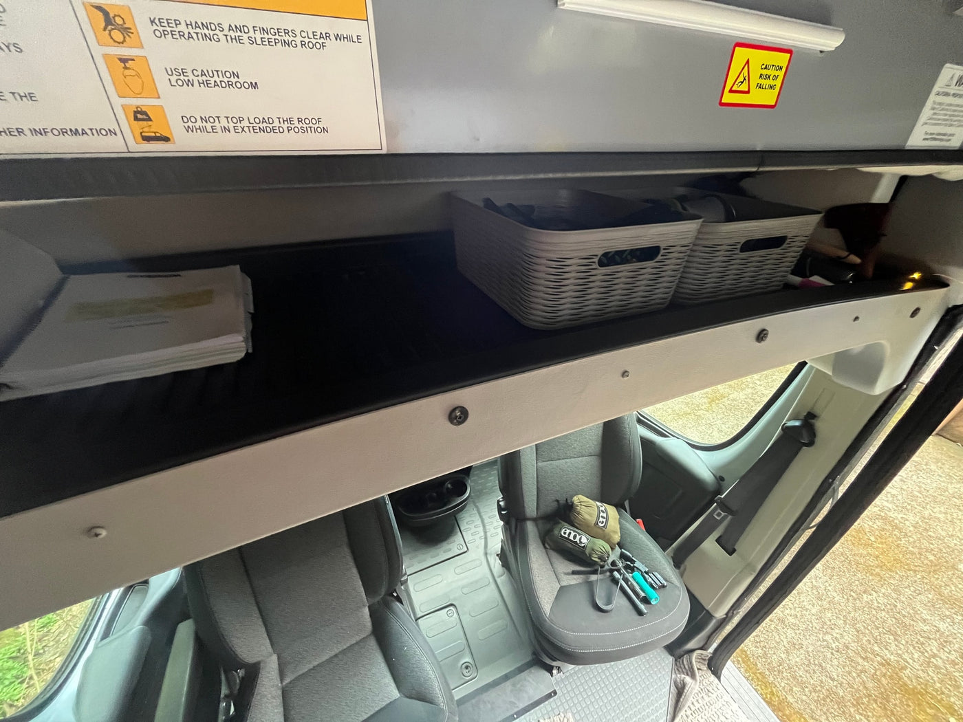 RV rental camper van interior: overhead storage with baskets, safety warnings for the sleeping roof, and front seats. — photo 19