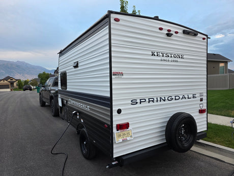 A Keystone Springdale RV rental with temporary Utah registration, hooked to a truck and plugged in, mountains behind.