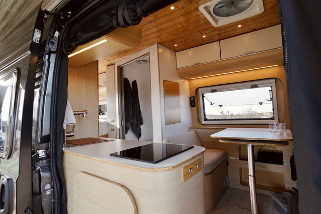 Step inside this chic rv rental: a bright camper van interior with a sleek kitchen, dining area, and a compact bathroom.