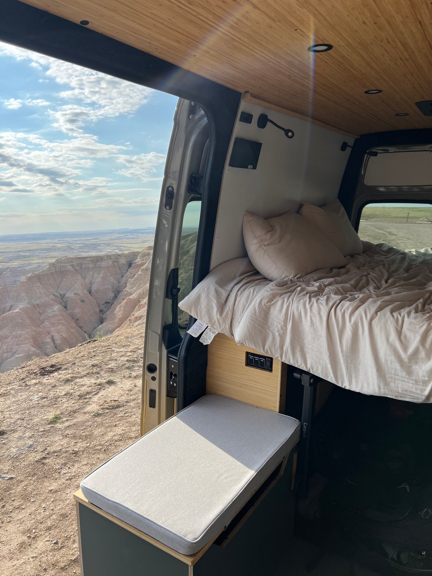 Inside a cozy RV rental: bed, bench, and open doors to a breathtaking badlands view. Perfect for van life adventures.