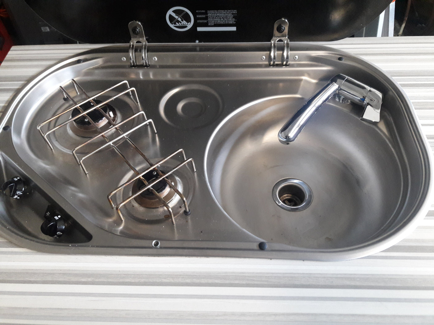Compact stainless steel sink, faucet, and two-burner cooktop in an RV rental kitchen. Ideal for travelers.