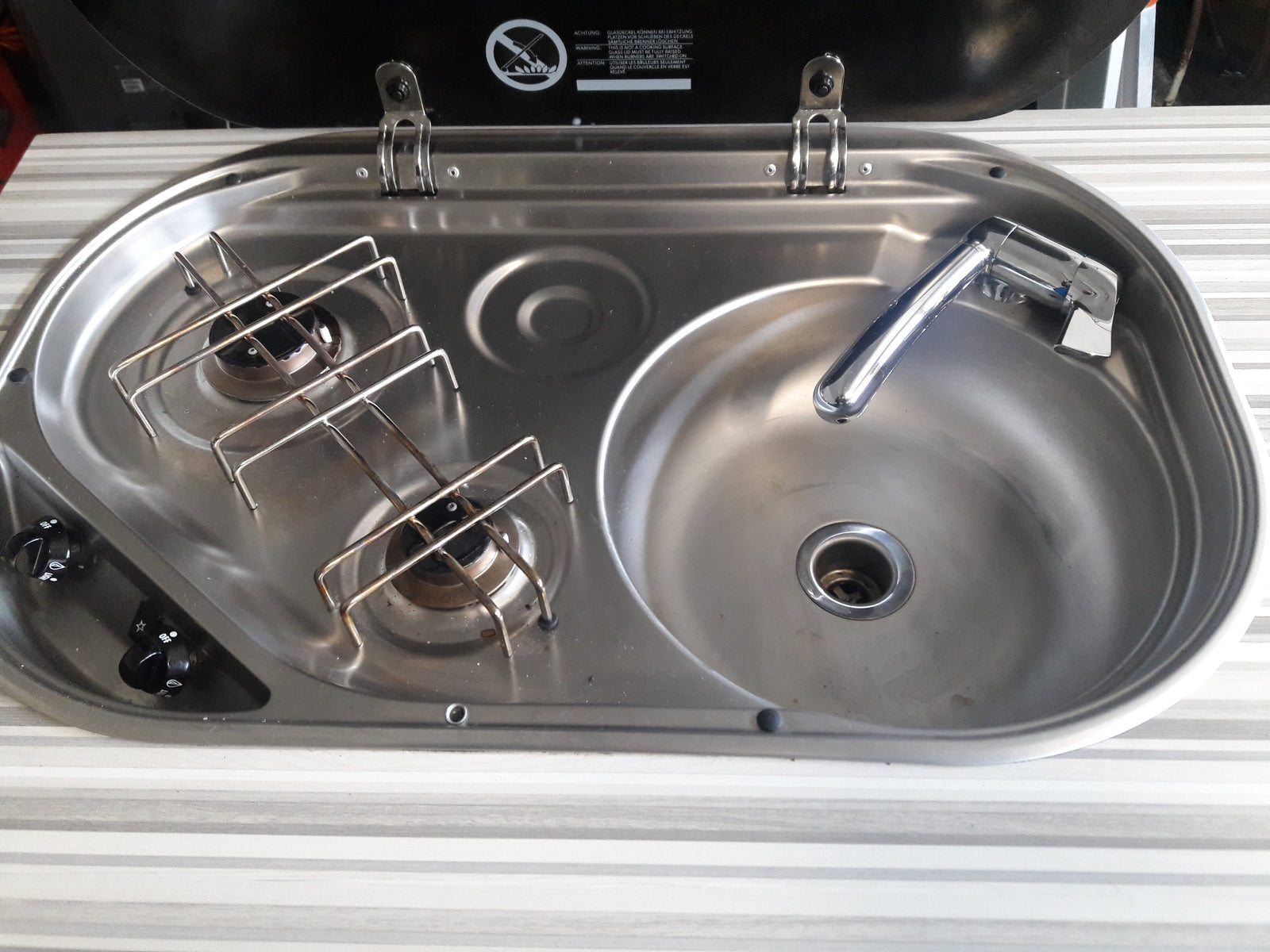 Compact stainless steel sink, faucet, and two-burner cooktop in an RV rental kitchen. Ideal for travelers.