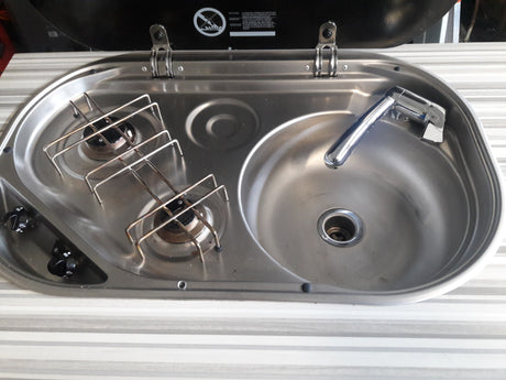 Compact stainless steel sink, faucet, and two-burner cooktop in an RV rental kitchen. Ideal for travelers.
