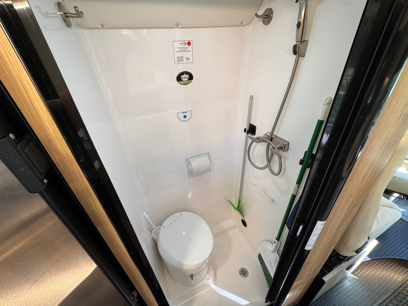 **rv rental** wet bath: a white toilet, wall-mounted shower, and cleaning tools neatly arranged in a compact space. — photo 16