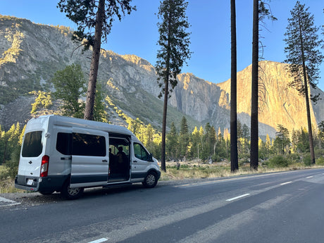 RV rental van parked roadside in Yosemite National Park, offering stunning mountain views and an open door for nature exploration.