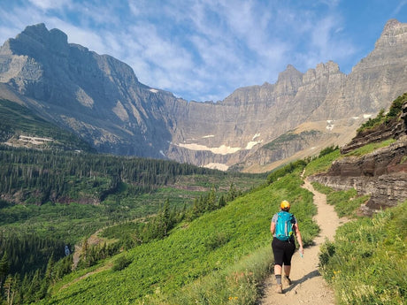 Discover majestic mountains & winding trails by RV rental! A hiker ascends a scenic path surrounded by lush greenery.