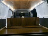 View of an RV rental van interior, featuring a wooden ceiling, bright LED lights, and a custom dark wood bed setup.