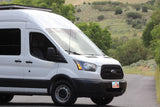 A white Ford Transit van, perfect for rv rental adventures, parked on a scenic road in Utah with green hills.