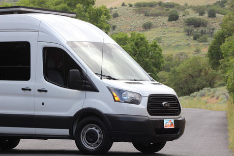 A white Ford Transit van, perfect for rv rental adventures, parked on a scenic road in Utah with green hills.
