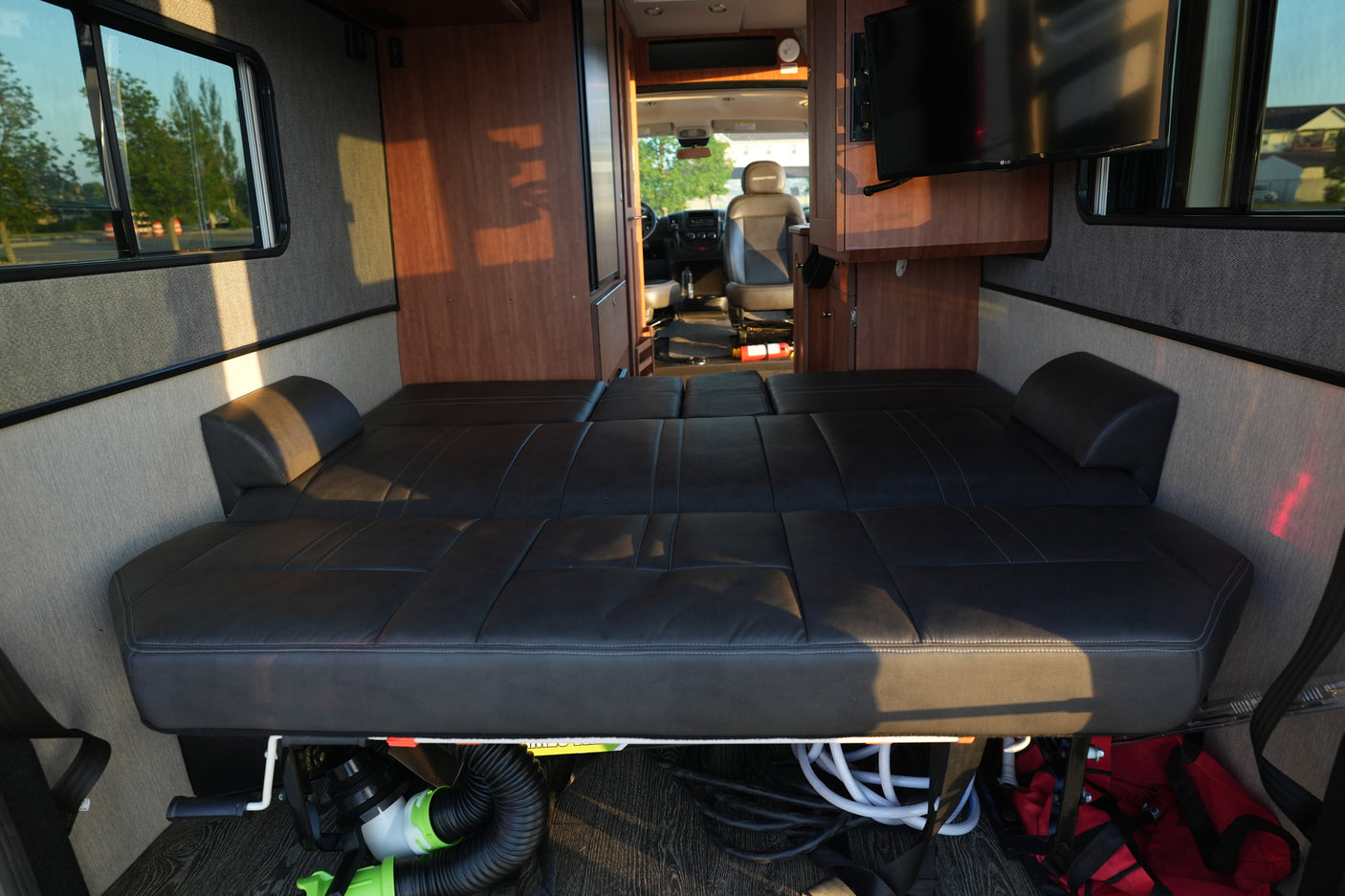Inside this rv rental, a comfortable black bed (convertible seating) stretches towards the front, with wood cabinets, a TV, and driver's cabin visible.