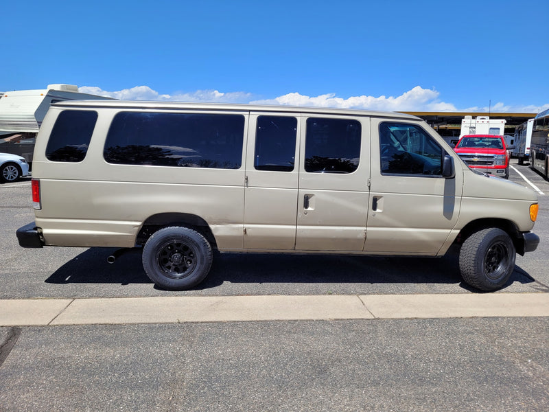 Tan Ford van with all-terrain tires, possibly an RV rental service vehicle, parked next to RVs under a blue sky. — photo 9