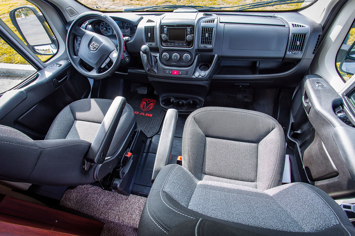 Spacious front cab of an RV rental van, showing the steering wheel, dashboard, seats, and infotainment system.