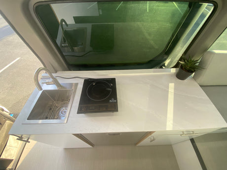 Modern RV rental kitchen with a stainless steel sink, induction cooktop, and sleek white counters for easy mobile living.
