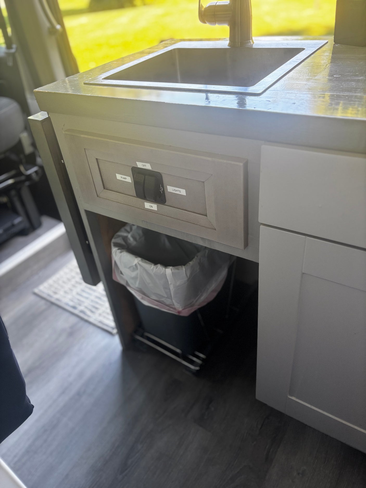 Compact RV rental kitchen with sink, faucet, trash can, and control switches for pump & lights. Ideal for mobile living.