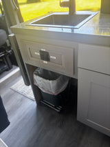 Compact RV rental kitchen with sink, faucet, trash can, and control switches for pump & lights. Ideal for mobile living.
