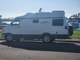 White RV rental parked seaside on a sunny day. Palm trees, sparkling ocean, and a boat provide a perfect travel backdrop.