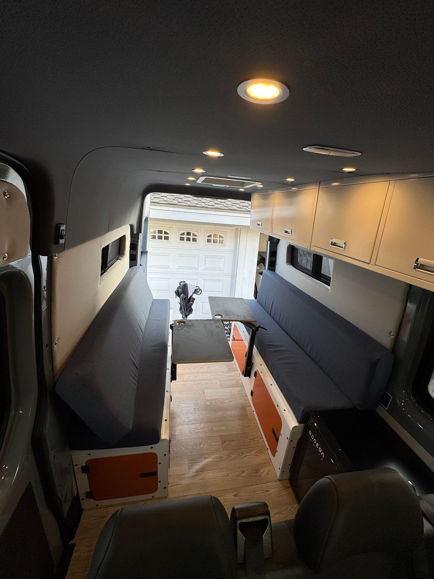 Inside a custom rv rental van conversion: comfortable living area with opposing cushioned benches, adjustable table, and overhead storage.
