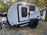 This light grey Bushwhacker teardrop camper makes a great RV rental, parked on gravel for outdoor adventures.