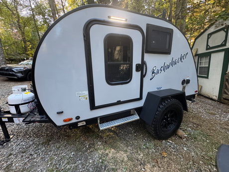 This light grey Bushwhacker teardrop camper makes a great RV rental, parked on gravel for outdoor adventures.