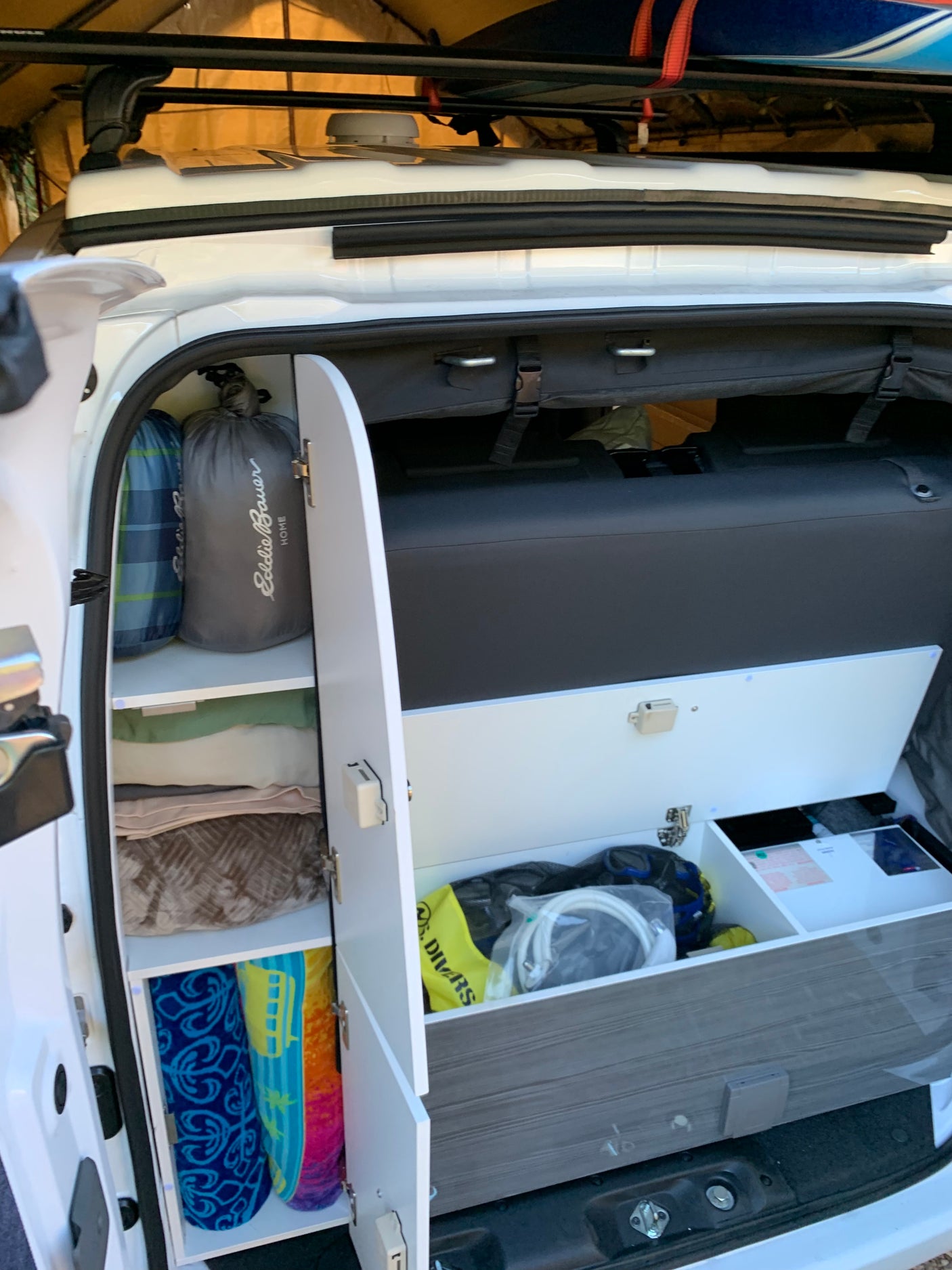 Organized RV rental: A look inside a camper van's custom storage with sleeping bags, blankets, towels, and road trip gear.