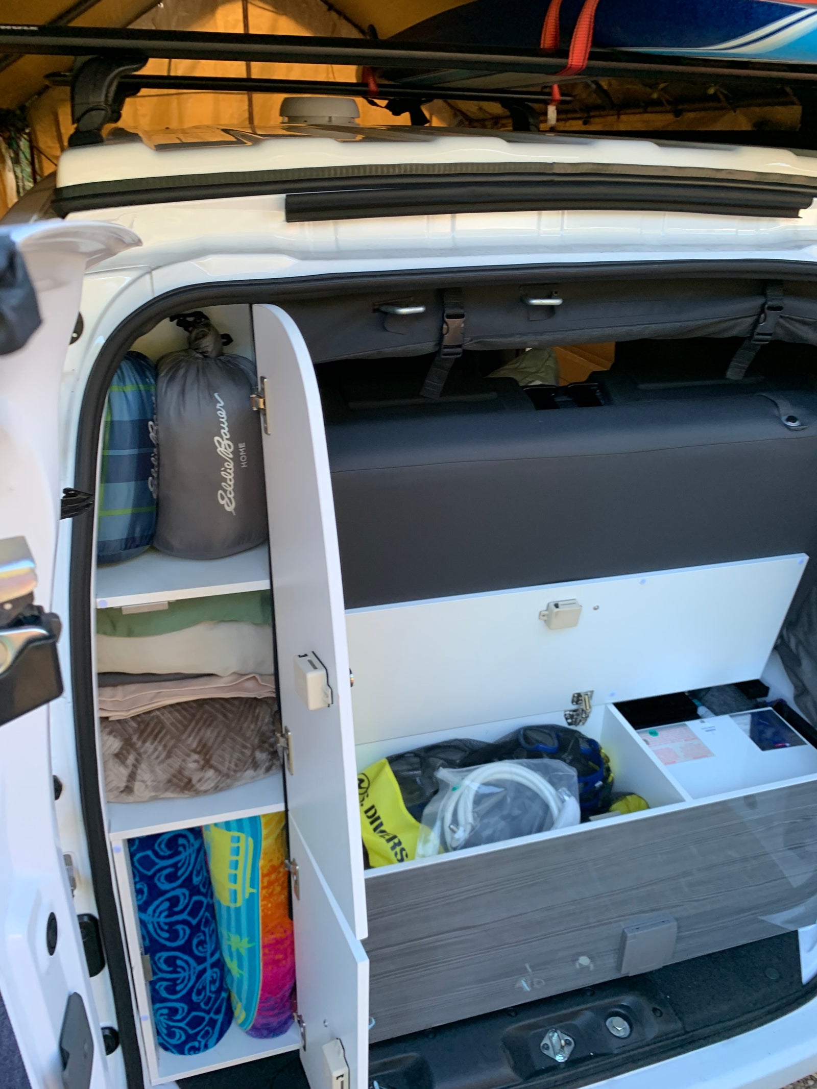 Organized RV rental: A look inside a camper van's custom storage with sleeping bags, blankets, towels, and road trip gear.