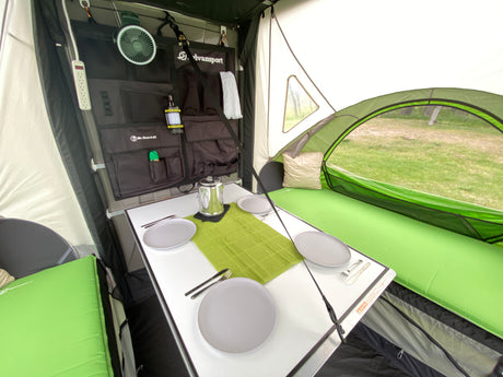 Organized RV rental interior features dining table, comfy sleeping pads, and wall storage for camping.