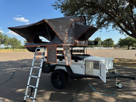 Explore with this rv rental! A compact camping trailer features a deployed rooftop tent, ladder, and open storage.