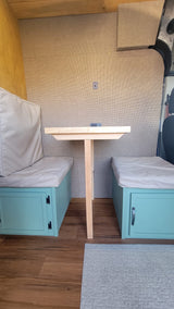 RV rental interior: Cozy camper van dining nook with teal bench seats, a wooden table, and wall power outlet.