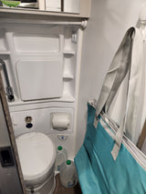 Compact RV rental bathroom: features a shower, Thetford portable toilet, and overhead storage. Ideal for travel.
