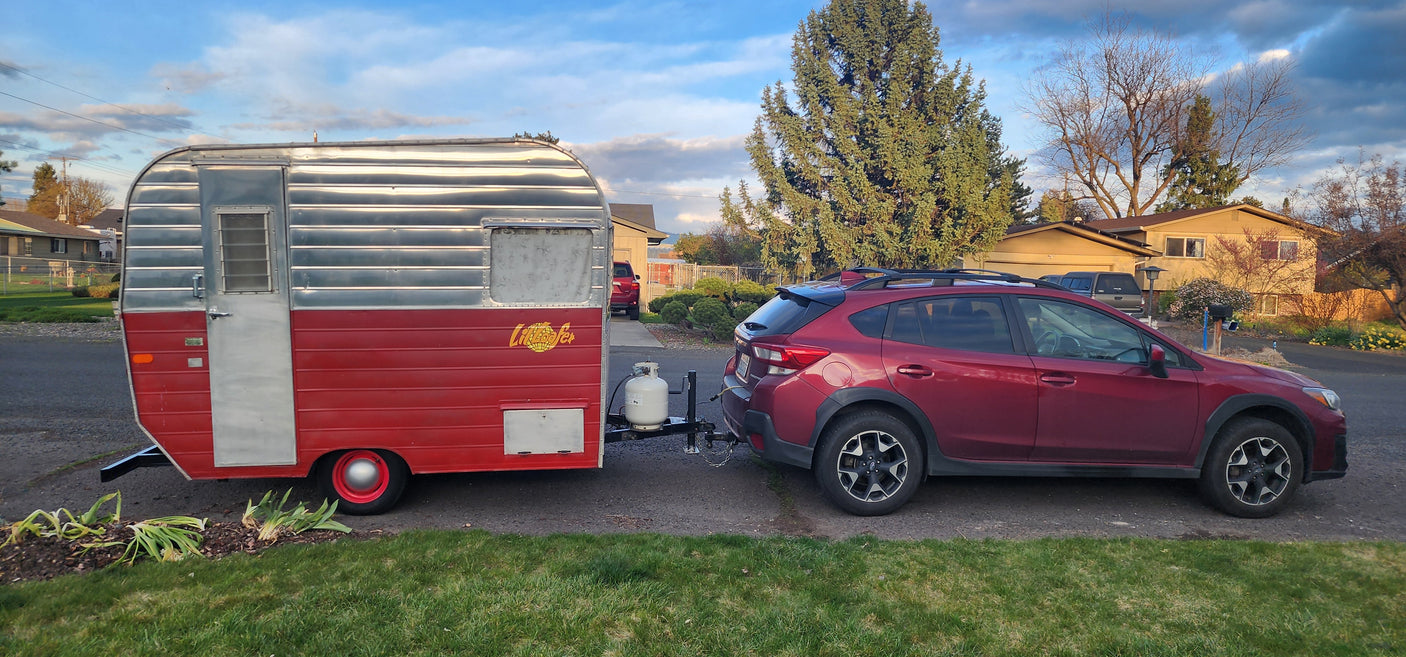 Red Subaru towing a vintage "Little Loafer" travel trailer, perfect for an RV rental adventure.
