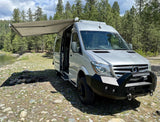 Your next rv rental adventure awaits! Silver Sprinter van parked by a river, awning out, fire pit ready for camping.