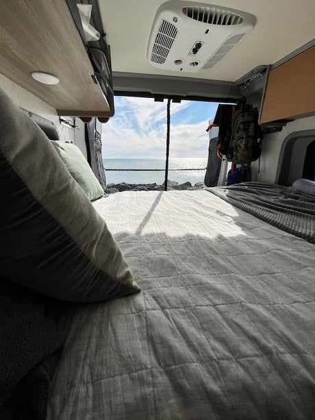 Inside a spacious rv rental, a comfortable bed offers stunning ocean views through the open rear doors. Ideal for travel.