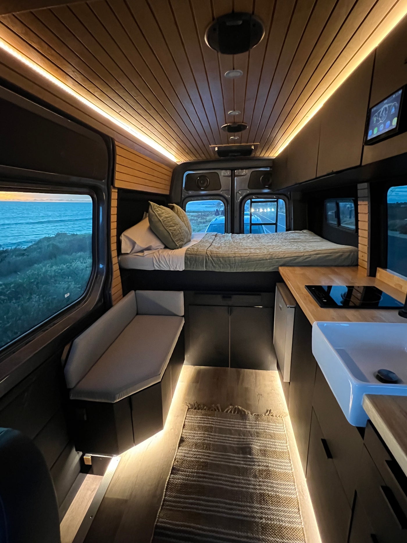Cozy RV rental interior with a comfortable bed, kitchen, seating, and scenic ocean views, ideal for a road trip. — photo 12