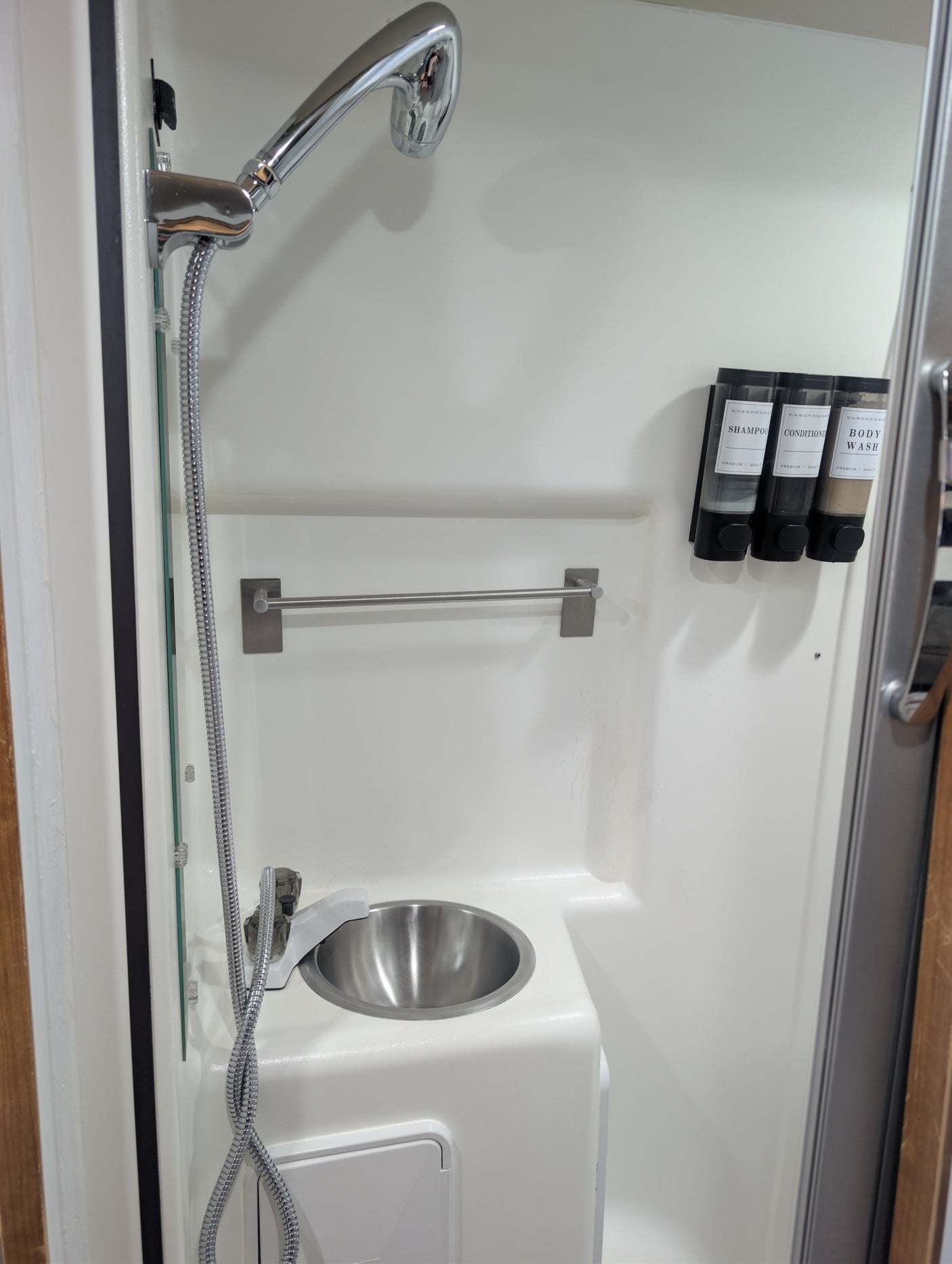 Compact RV rental bathroom features: shower, small sink, and wall-mounted shampoo, conditioner, and body wash dispensers.