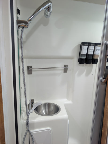 Compact RV rental bathroom features: shower, small sink, and wall-mounted shampoo, conditioner, and body wash dispensers.