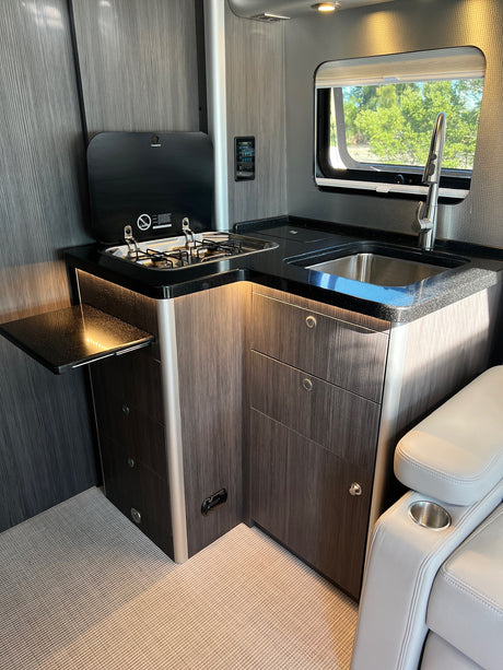 RV rental's compact, modern kitchen: Dometic stovetop, sink, and dark wood-grain cabinets with LED accent lighting.