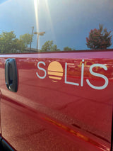 Red Solis RV rental side with sun-like logo, door handle, and blue sky reflection in window.