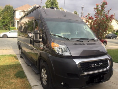Dark grey Ram ProMaster RV camper van rental parked on a driveway with houses and trees in the background.