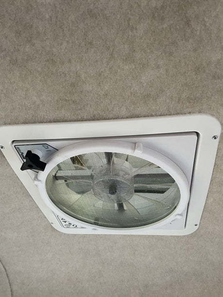 An RV rental features a Maxx-Fan ceiling vent with screen, offering fresh air. Light grey upholstered interior.