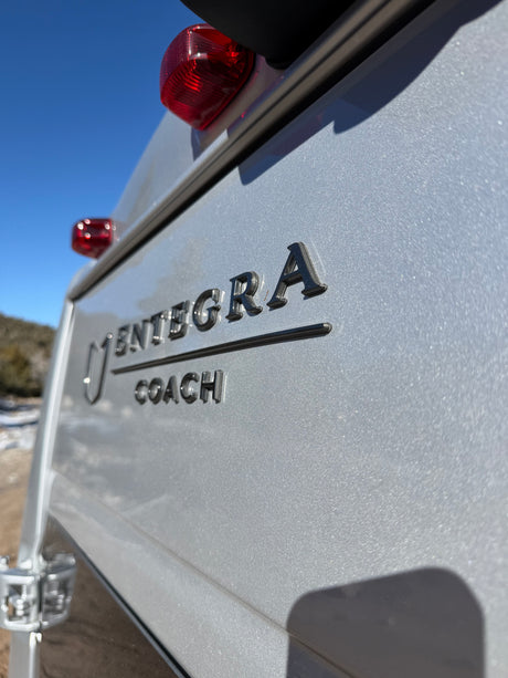 Close-up of a silver Entegra Coach RV's rear, featuring raised brand letters and red taillights. Great for your next rv rental journey.