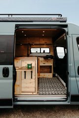 Stylish RV rental interior with custom wood, kitchen area, foldable table, and a patterned rug. Adventure awaits!
