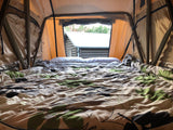 Cozy rv rental interior: A comfortable bed with a view of a cabin from inside a rooftop tent.