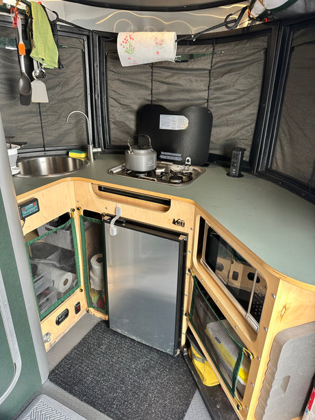 Compact RV rental kitchen features sink, stove, microwave, and fridge, optimizing space for travel cooking and convenience.